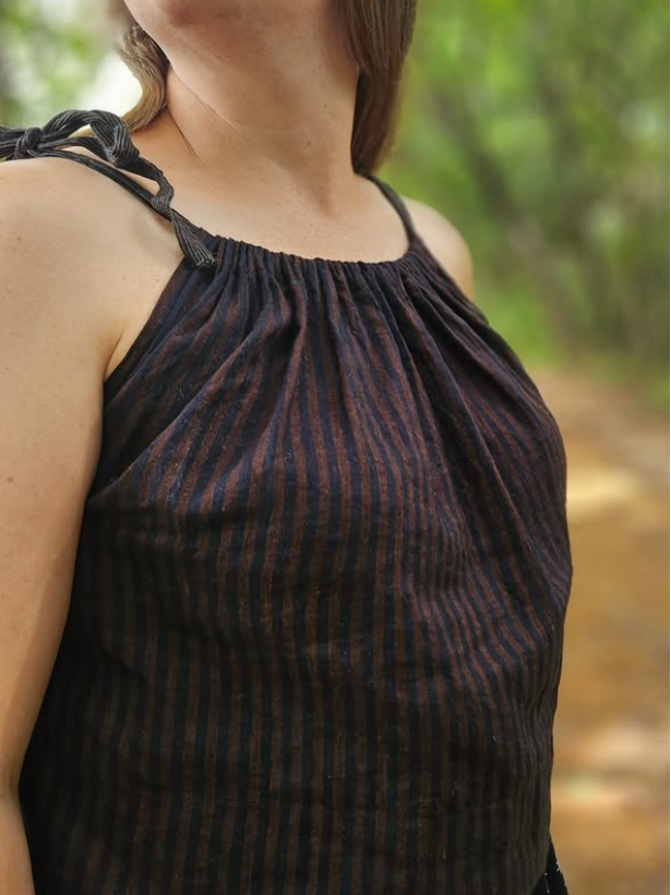 Woman wearing a dark striped sleeveless top with blurred greenery in the background